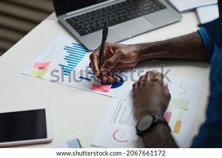 Close up of young African-American man working at desk in office and writing notes, copy space