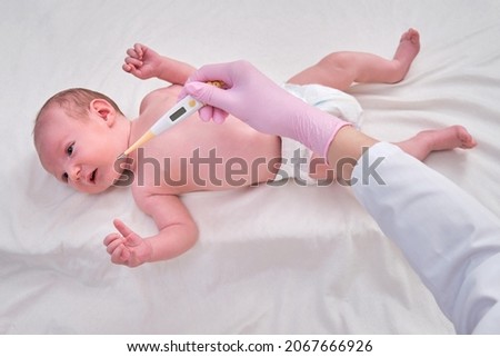 Doctor checks the temperature of the newborn baby with a thermometer. A nurse in uniform measures the child fever with a thermometer