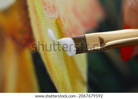 Close-up of female painter creating new picture. Artist using paintbrush with white paint. Creative atmosphere in studio. Tool for work. Art and creativity concept