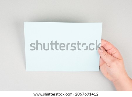 Woman holds a blank sheet of paper, grey colored background, empty copy space for text