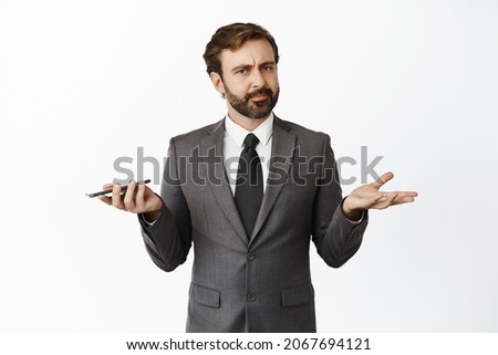 Whats wrong. Clueless businessman shrugging shoulders while holding cellphone, cant understand, dont know, standing over white background