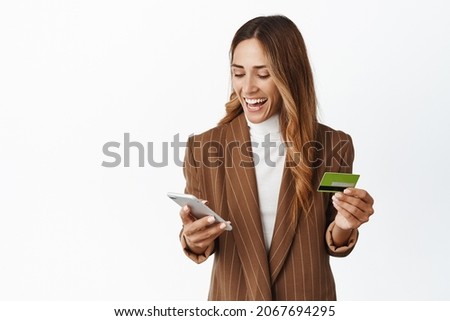 Happy corporate woman order online on smartphone app, holding credit card and smiling at mobile phone, white background
