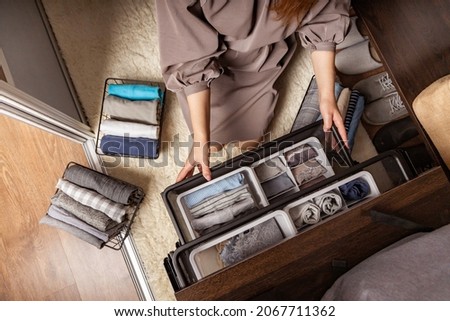 Housewife hands with neatly put underwear, clothes and accessories modern wardrobe organization top view. Woman arms carrying ecological minimalist clothing box container storage Marie Kondo method