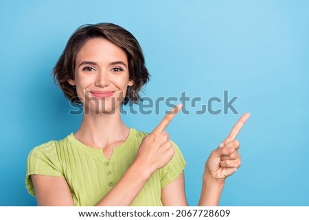 Photo of pretty charming young lady wear green t-shirt pointing two fingers empty space isolated blue color background