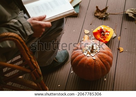 Romance of autumn poetry. A man sits in a wicker chair and reads a book. Next to the floor is a round pumpkin and a stack of books
