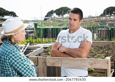Elderly woman and young man talking on the border of the garden plot. High quality photo