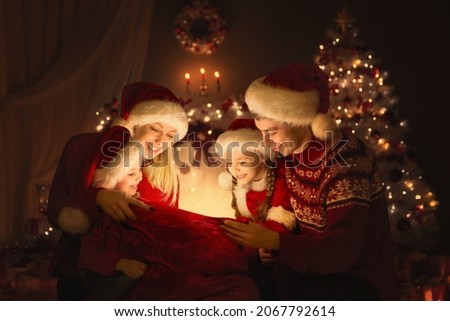 Christmas Family opening Santa Bag with Gifts. Happy Parents and Kids sitting in front of Decorated Xmas Fir Tree and looking at Magic Light. Winter Holiday Eve