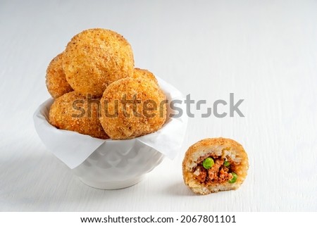 Tasty homemade Arancini Italian or Sicilian rice balls stuffed with minced meat, tomato sauce and green peas, coated with bread crumbs and deep fried, served in bowl with paper on white wooden table Royalty-Free Stock Photo #2067801101