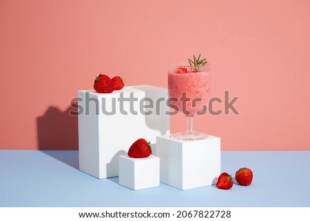 Pink Background with strawberry smoothie in a cocktail glass and strawberries and white podium in . Production of cosmetics based on strawberry. Blank space for advertising