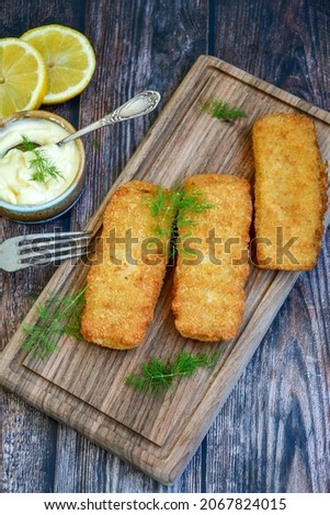 Close up of   Crispy breaded  deep fried fish fingers with breadcrumbs served  with remoulade sauce and  lemon Cod Fish Nuggets on rustic wood table background