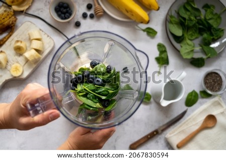 Cooking, preparring green spinach, banana and blueberry smoothie. Female hands, top view. Step by step photos.