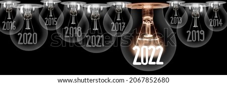 Horizontal group of shining light bulb with fiber in a shape of New Year 2022 and dark light bulbs with years passed isolated on black background.