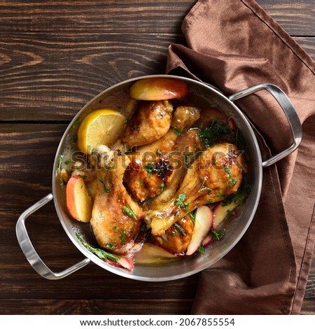 Close up view of chicken drumsticks baked with apples and herbs on wooden background. Top view, flat lay