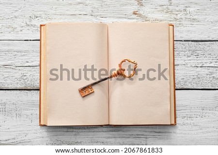 Open old book with key on light wooden background