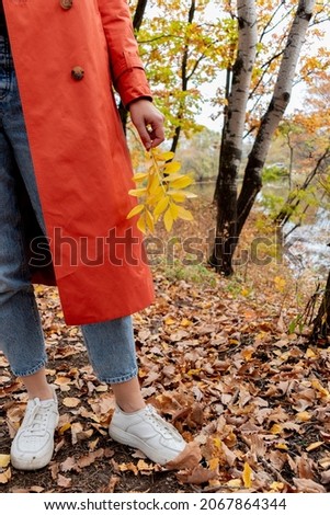 Young girl with blond hair walks in the autumn forest. Wellness concept. Orange trench coat and black hat. Copy space