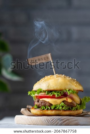 Classic burger with paper flag with lettering and smoke on chalkboard, close-up