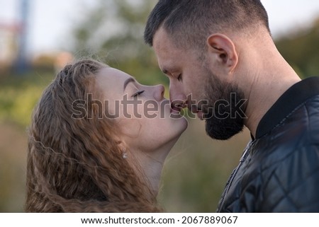 Attractive Caucasian couple. Close-up portrait of wife kissing husband on nose on autumn day outdoors. Young man and woman are happy. Love, tenderness, relationship, romance. Royalty-Free Stock Photo #2067889067
