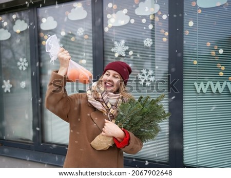 profile view of a young modern girl in winter clothes with fir branches in her hands on the background of a Christmas showcase.Holiday concept.New Year celebration