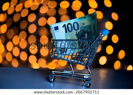 Christmas shopping online.Trolley with 100 euro notes on the background of blurred bokeh lights.