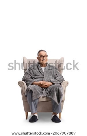 Mature man in a bathrobe and pajamas sitting in an armchair isolated on white background Royalty-Free Stock Photo #2067907889