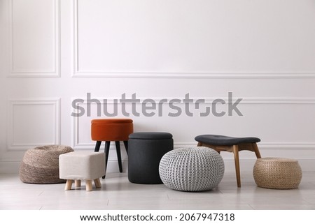 Different stylish poufs and ottomans near light wall Royalty-Free Stock Photo #2067947318