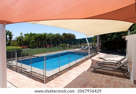 Fenced swimming pool in garden with sunbeds under a shade sail Royalty-Free Stock Photo #2067956429