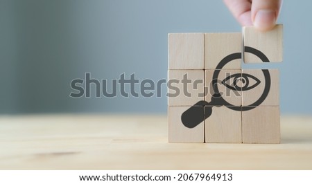 Search, Research, Finding Solution, Investigate Concept. Hand holds the wooden cubes with magnifying glass with eye symbols on grey background, copy space. Marketing research. Customer insight. SEO. Royalty-Free Stock Photo #2067964913