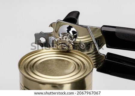 A can opener opening a can of food. Kitchen utensils, close-up. Royalty-Free Stock Photo #2067967067