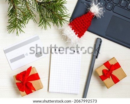 Christmas online shopping flat lay. Notebook with pen. Shopping list. Credit card, Laptop, Christmas tree and presents on white table. Page for your write. Top view copy space. Winter holidays sales