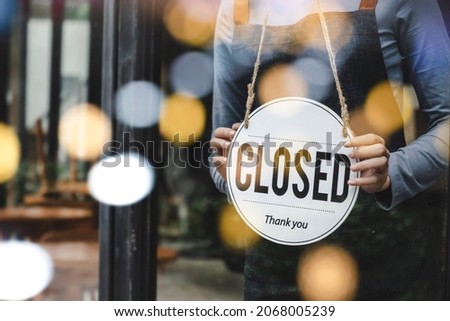 asian waitress staff woman wearing apron turning CLOSED sign board on glass door with bokeh light in modern cafe coffee shop, cafe restaurant, retail store, small business, food and drink concept