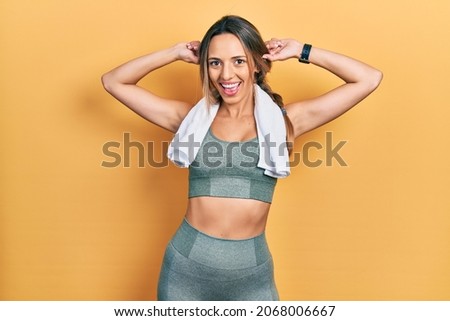 Beautiful hispanic woman wearing sportswear and towel smiling pulling ears with fingers, funny gesture. audition problem 