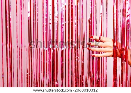 Beautiful woman hand with nail polish in red breaking through a pink tinsel. Ready for special party. Royalty-Free Stock Photo #2068010312