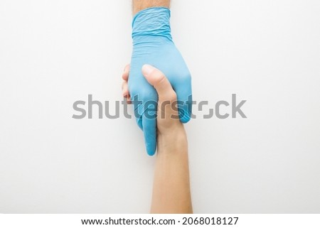 Doctor hand in rubber glove shaking young adult woman hand on white table background. Closeup. Grateful patient thanking to medical specialist at office. Medicine, healthcare and trust concept. Royalty-Free Stock Photo #2068018127