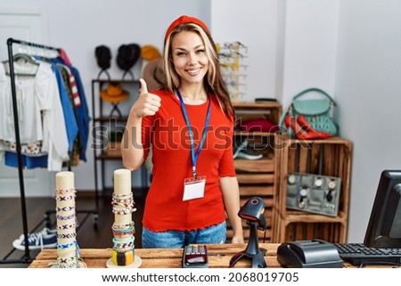 Young caucasian woman working as manager at retail boutique smiling happy and positive, thumb up doing excellent and approval sign 