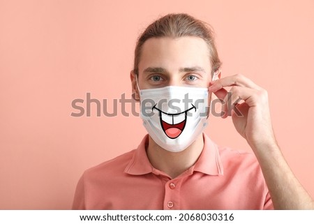 Man wearing medical mask with drawn smile against color background