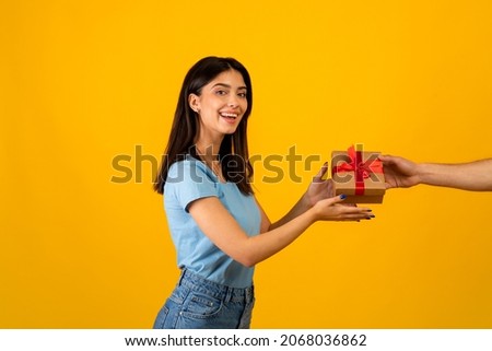 Presents delivery, holiday celebration concept. Excited arab lady receiving wrapped gift box, standing over yellow studio background and smiling to camera