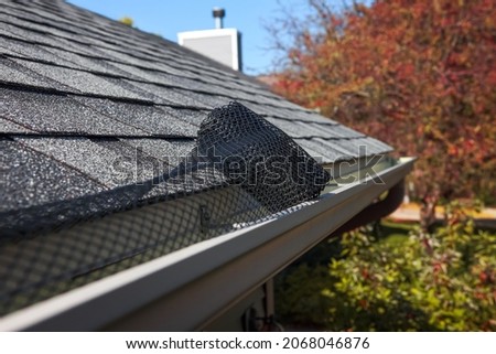 Roll of plastic mesh guard over gutter on a roof to keep it free from leaves and debris, shallow focus on roll of mesh Royalty-Free Stock Photo #2068046876