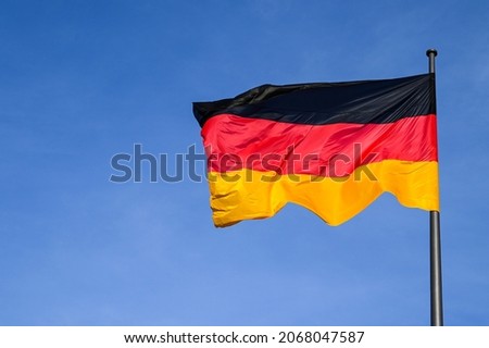 German flag flying on the wind. Waving flag of Germany on flagpole against blue sky. Deutschland. Black, red and yellow colors on German flag in a front of Bundestag. Symbol of German people. 