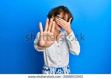 Young brunette woman wearing casual clothes and glasses covering eyes with hands and doing stop gesture with sad and fear expression. embarrassed and negative concept. 