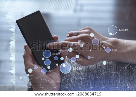 Trader holding in the hands a smart phone and researching stock market to proceed right investment solutions. Internet trading and wealth management concept. Hologram Forex chart over close up shot.