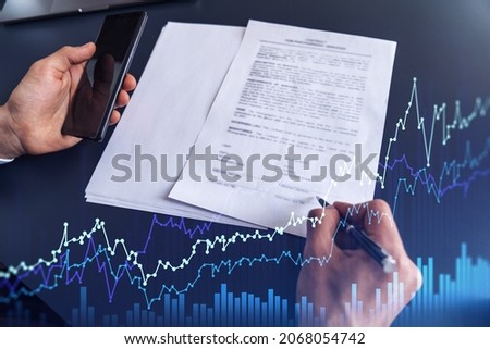 A client in formal wear is signing the contract to invest money in stock market. Internet trading and wealth management concept. Forex and financial hologram chart over the desk.