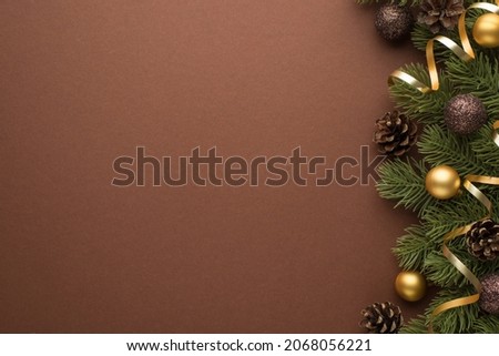 Top view photo of gold and brown christmas tree balls cones and serpentine on pine branches on isolated brown background with copyspace