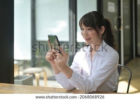 Photo of a beautiful woman using a smartphone while sitting at the wooden working in the comfortable living room.