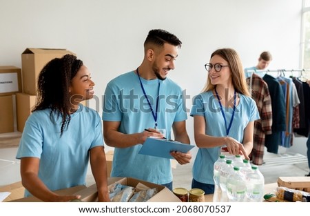 Arab male manager checking donation list and writing in clipboard. Diverse volunteer workers working in shipping delivery charitable stock organization packing donations boxes Royalty-Free Stock Photo #2068070537