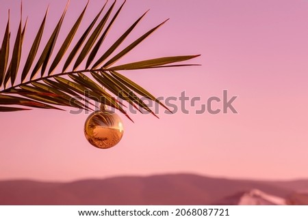 Christmas decorations bauble golden ball on palm twig over sea during sunset. Ocean beach - Christmas and New Year holidays in hot countries concept. Greeting card. Copy space