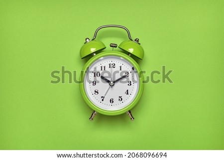 Green alarm clock on light green background. Top view, flat lay, copy space.