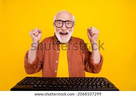 Photo of champion grandpa sit computer raise fists scream goal wear specs brown shirt isolated yellow color background