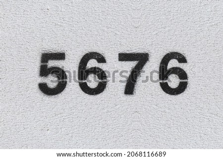 Black Number 5676 on the white wall. Spray paint. Number five thousand six hundred and seventy six.