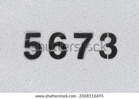 Black Number 5673 on the white wall. Spray paint. Number five thousand six hundred and seventy three.
