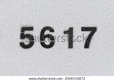Black Number 5617 on the white wall. Spray paint. Number five thousand six hundred and seventeen.